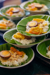 Several portions of authentic Indonesian food, Nasi Liwet or Nasi Ayam, white rice with shredded chicken, marinated egg, and vegetables served on banana leaf. Traditional Asian communal dining concept