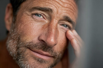 Fototapeta premium Close-up portrait of a rugged man with stubble, touching his temple with a pensive gaze, revealing textured skin and a subtle, introspective mood.