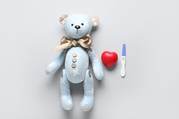 Toy bear with pregnancy test and heart on grey background. IVF concept