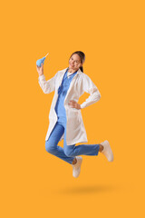 Young happy female doctor with enema jumping on yellow background