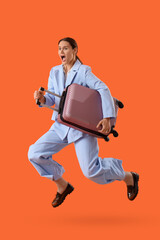 Young shocked businesswoman with suitcase jumping on orange background