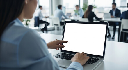 Young business woman working on laptop with blank copy space screen for ad app in modern busy office. Over shoulder view on businesswoman using touchscreen of a computer with white mockup monitor.