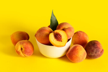 Bowl with sweet ripe peaches on yellow background