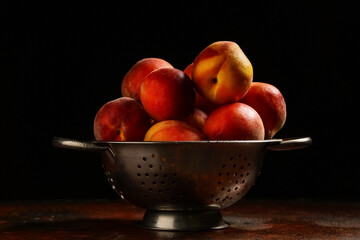 Colander with sweet ripe peaches on dark table