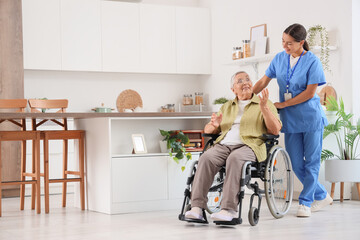 Female caregiver helping happy senior woman in wheelchair at kitchen