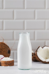 Fresh coconut milk in glass bottle with whole and halved coconuts. Vegan healthy milk