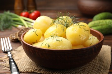 Tasty young boiled potatoes with dill and oil in bowl on wooden table, closeup