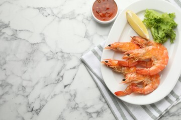 Delicious seafood dish. Tasty grilled shrimps served with lemon, lettuce and sauce on white marble table, flat lay. Space for text