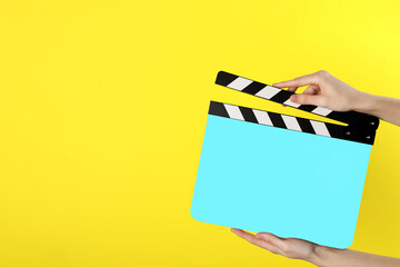 Woman holding cyan clapperboard on yellow background, closeup with space for text. Film industry