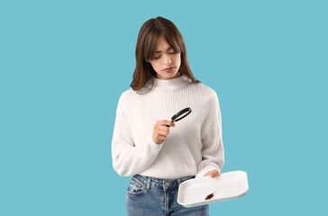 Young woman with cockroach in tray and magnifier on blue background