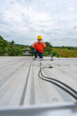 Obraz premium Technician in safety uniform and helmet kneeling on a rooftop, using a drill for precise installation work. A scene highlighting safety, professionalism, and technical expertise in construction.