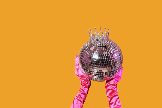 Female hands in gloves with disco ball and tiara on orange background