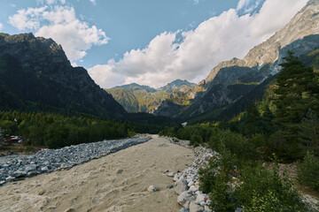 A rugged mountain landscape features a rocky riverbed and a wide valley, with towering cliffs and clear skies, evoking adventure, solitude, and pristine nature.