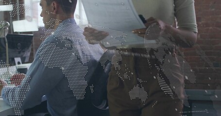 Collaborating analyst and manager reviewing reports on monitor at office, with world map overlay