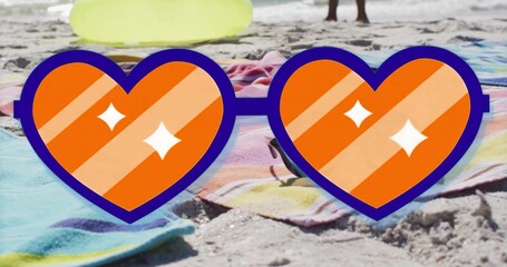 Resting novelty heart-shaped sunglasses on pastel beach towels at shoreline, with yellow swim ring