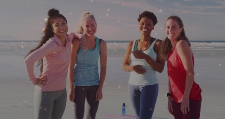 Smiling women exercising in sportswear at beach shore, with pink exercise mat and blue water bottle