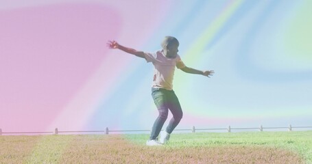 Balancing boy wearing pink shirt and jeans on grassy slope, with metal railing and pastel sky