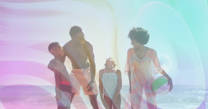 Smiling family wearing swimwear standing on sandy shore near water, holding green white beach ball