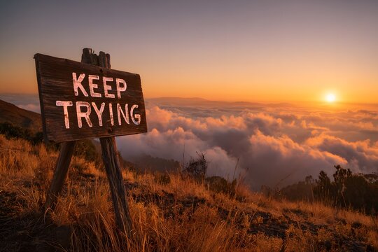 Motivational keep trying sign on mountain at sunrise.