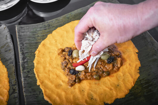 A chef's hands carefully assemble the ingredients for a hallaca