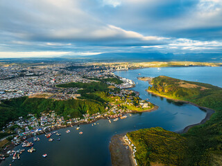 An aerial view of Puerto Montt Canal de Tenglo during the afternoon, with a mix of golden light and dramatic shadows on the landscape under a cloudy sky.