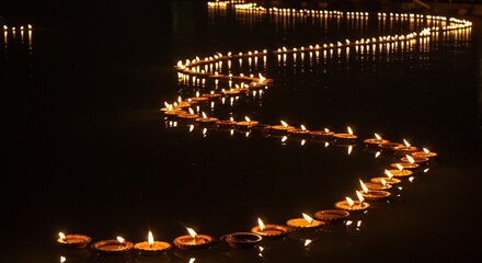 Obraz premium A winding row of small candlelit clay lamps floats on a dark body of water reflected in the still surface