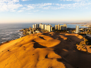 Aerial view of the striking Concón dunes at sunset, with the coastal city and the Pacific Ocean in the background.