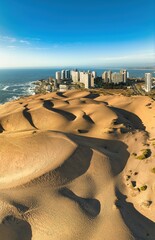 Vertical panoramic aerial view of the iconic Concón dunes and the city's urban skyline bathed in golden light.