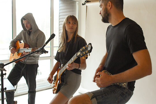 group of young people playing guitars and drums in a bright room - Powered by Adobe