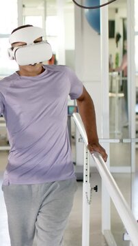 Balancing man gripping parallel bars at rehabilitation gym, with VR headset and therapy ball