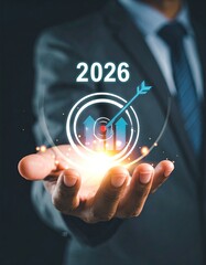 A businessman's hand holds a 2026 target graphic with upward arrows, signifying goal achievement
