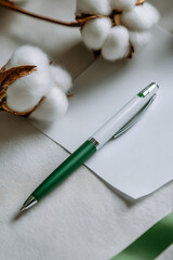 A green and white pen rests on a white notepad with cotton branches in the background