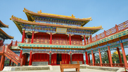 Naklejka premium Traditional Chinese temple in Penglai, Shandong, with red pillars, golden roofs, and ornate details, surrounded by lush greenery and a serene natural setting.