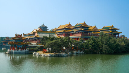 Naklejka premium Traditional Chinese temple in Penglai, Shandong, with red pillars, golden roofs, and ornate details, surrounded by lush greenery and a serene natural setting.