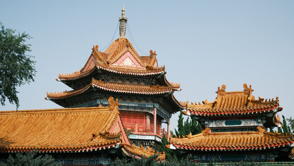 Naklejka premium Traditional Chinese temple in Penglai, Shandong, with red pillars, golden roofs, and ornate details, surrounded by lush greenery and a serene natural setting.