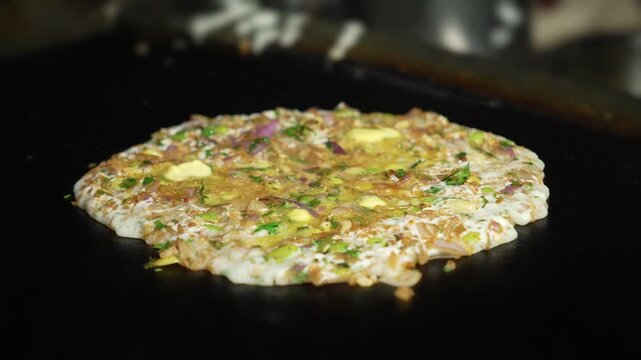 Close-up shot of onion dosa cooking with oil on hot tawa. Traditional Indian recipe.