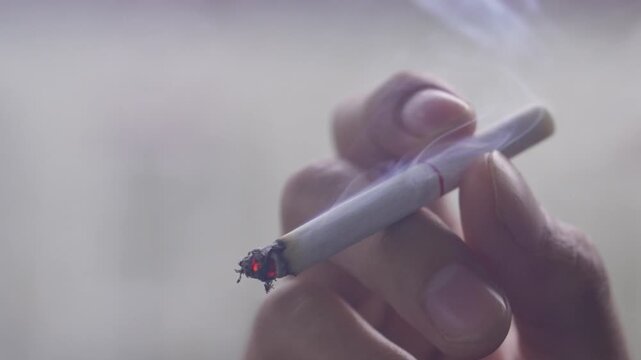 Close-up of a person smoking a cigarette, with smoke rising into the air, illustrating addiction, lifestyle, and health risk