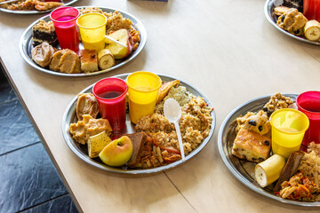 Vegetarian food portions including rice, sweets, fruits, and beverages are arranged on stainless steel plates. Meal is prepared as prasadam, sacred offering in Hindu practice, selective focus