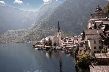 Fototapeta premium Idyllic Lakeside Village of Hallstatt, Austria, with Alpine Mountains and Church Steeple. The calm lake reflects the charming village and dramatic mountain backdrop, creating a serene and storybook.