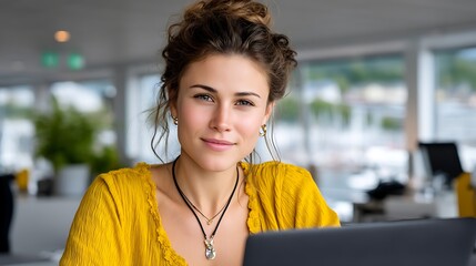Young woman with wavy hair wearing yellow top working on laptop in modern office