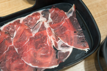 Raw sliced beef in black tray on wood table for sukiyaki