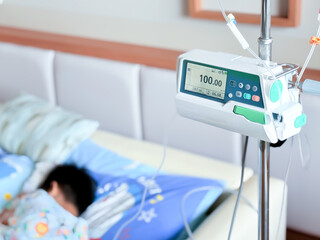 Medical infusion pump with digital screen displaying flow rate in a hospital room. Pediatric patient resting in bed in the background. Healthcare and intravenous therapy concept.