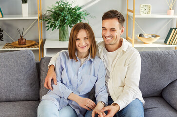 Home portrait of happy young married couple in love posing for photo seated on couch in modern...