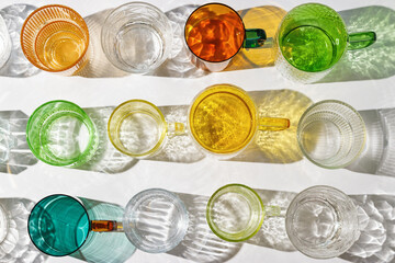 Set colored glass cups from transparent and clear glasses with beautiful shadow at sunlight, summer drink for events or relaxation, minimal aesthetic top view, creative summer drink backdround