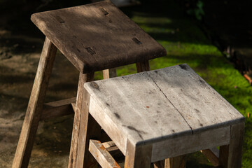 Fototapeta premium A rustic still life of two old, weathered handmade wooden stools sitting in a garden with a mossy background, representing simplicity and wabi-sabi aesthetics.