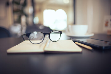 close up, eyeglasses on notebook with mobile phone, coffee cup, blure background, bokeh and vintage color tone