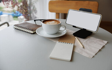 smart phone on stand with latte coffee, note book and diary on table