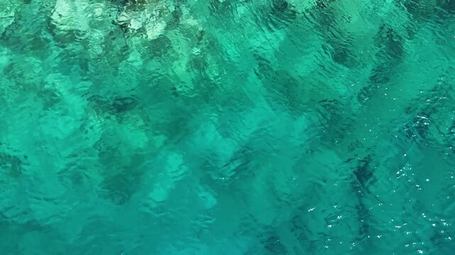 A mesmerizing top down drone video of a clear turquoise sea water showing rocks and marine plants on the seabed a beautiful and tranquil abstract nature background