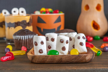 Marshmallow ghosts on traditional Halloween treat background.
