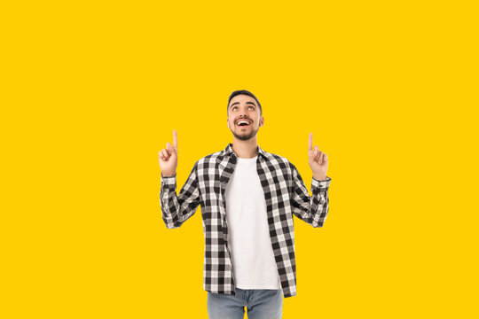 Cheerful young man points at something above him while smiling